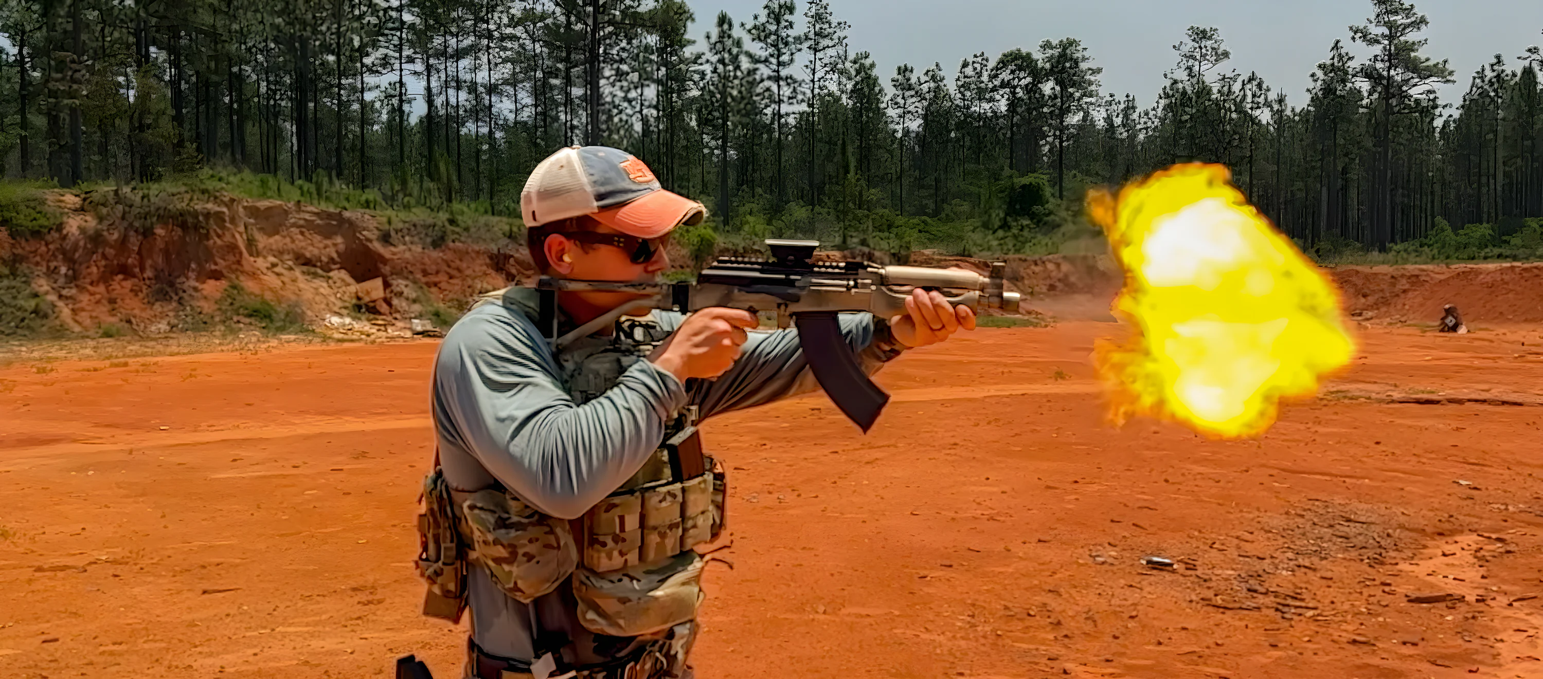 A shooter running an AK on a red-clay range with a full muzzle flash.